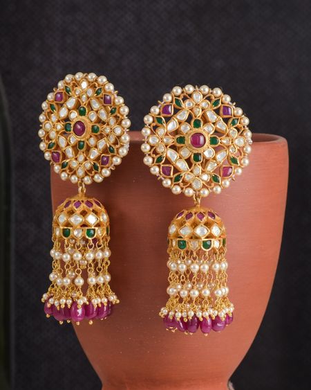 Large gold jhumkas with pearl and ruby detailing displayed on a terracotta pot