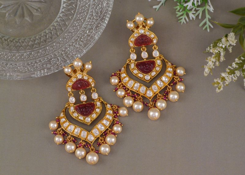 A pair of ornate gold-tone earrings with red details and white beads on a grey surface