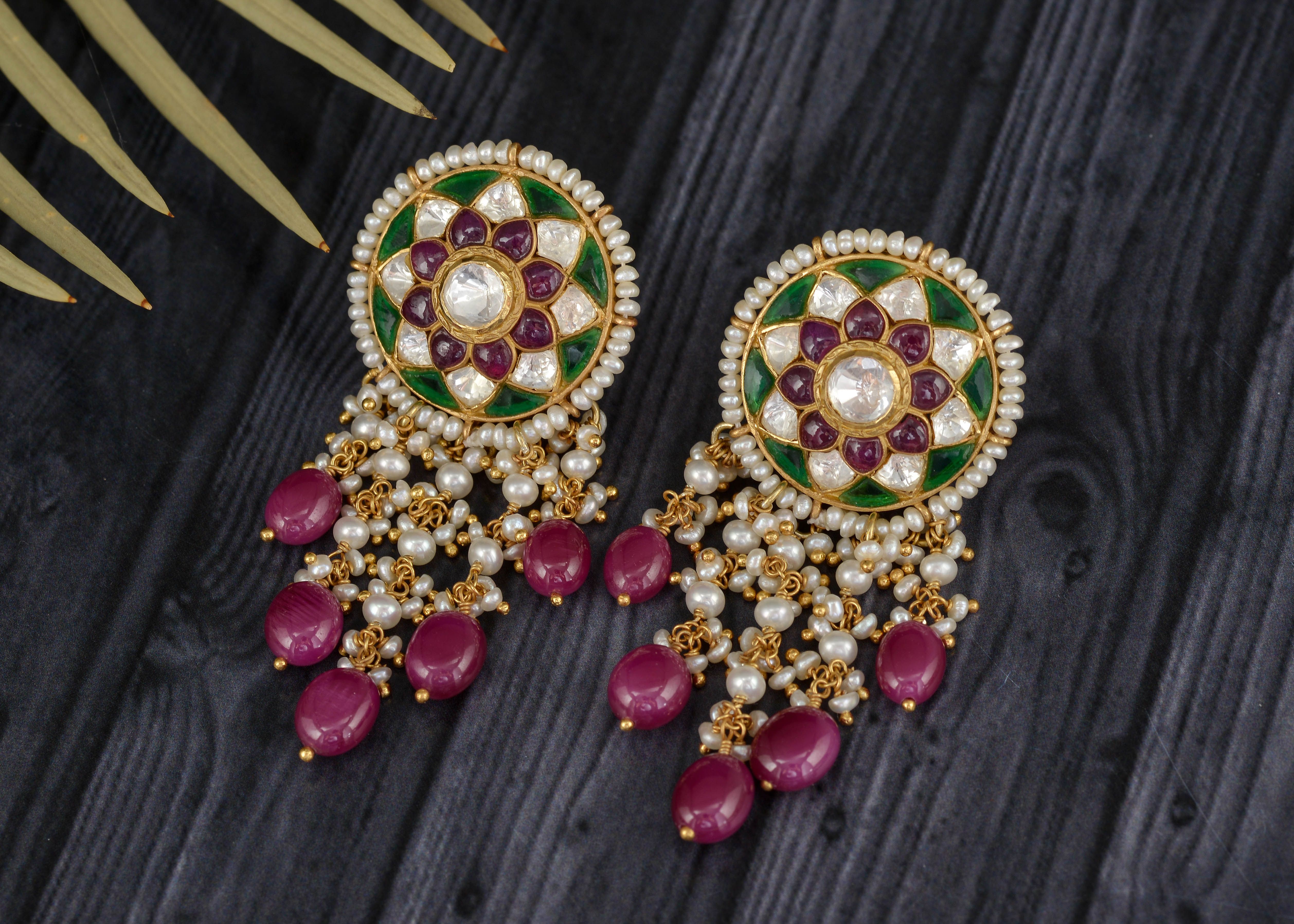 Close-up of colorful traditional Kundan earrings with pearls and beads on a wooden background.