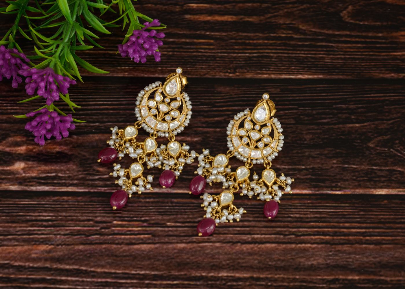Ornate chandbali crescent earrings with pearls and red stones on a wooden surface