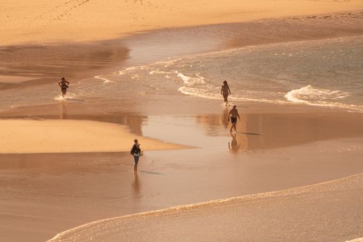 A serene beach scene with four people walking along the shoreline, waves gently lapping the sand.