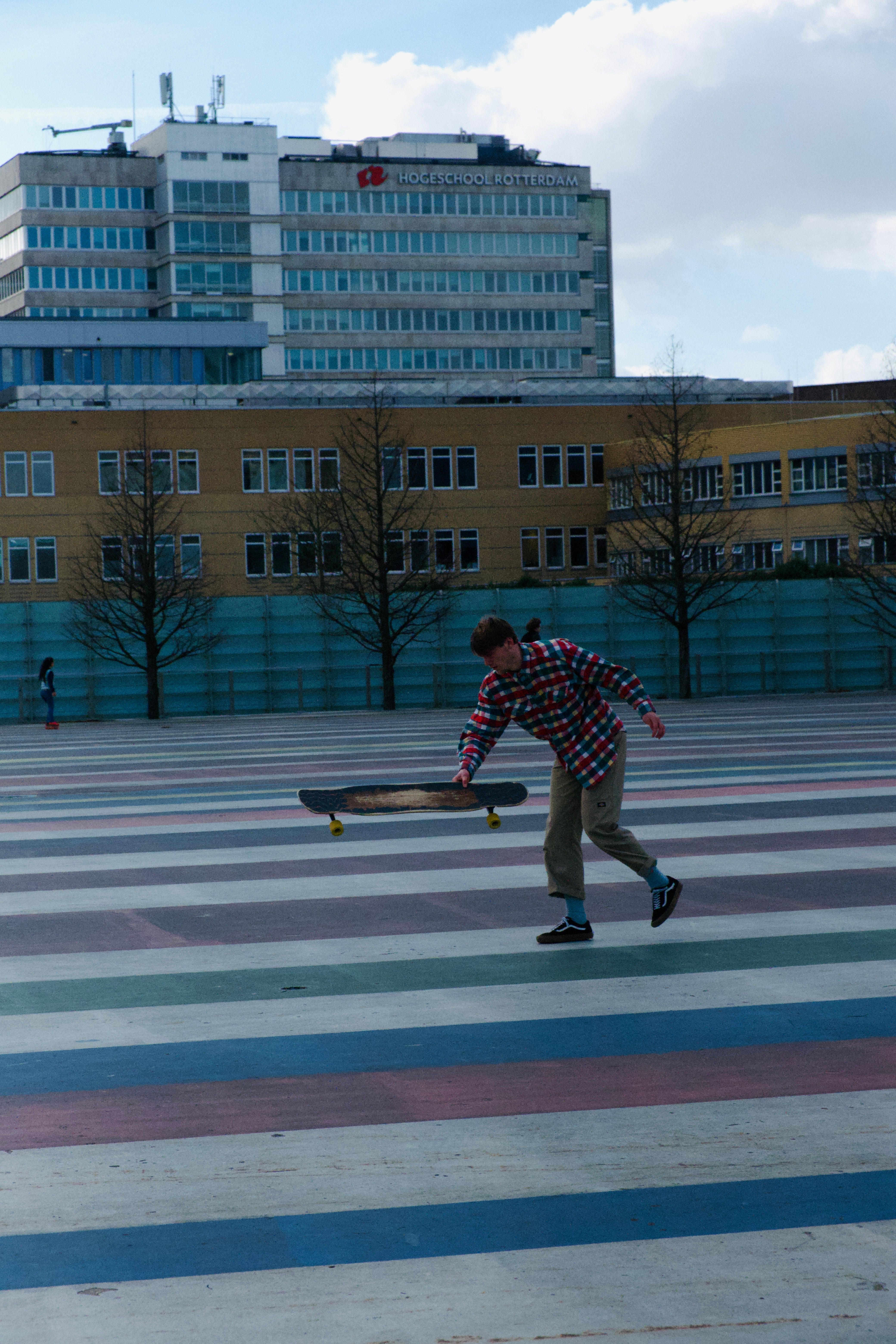 A young man in a plaid shirt skateboards at an outdoor urban park in daytime.