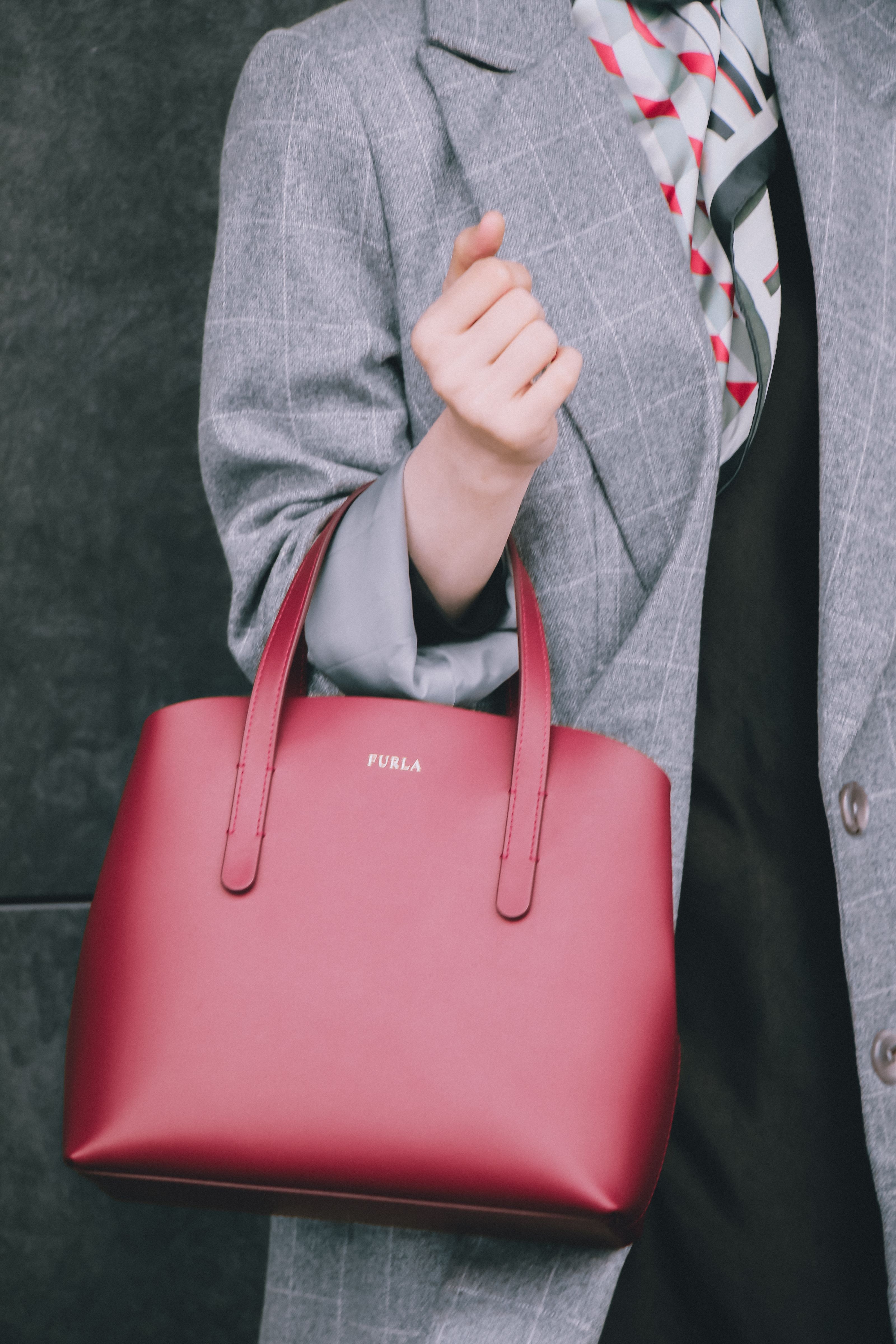 Mulher estilosa em um casaco cinza segurando uma bolsa de couro borgonha, mostrando a moda moderna de outono.