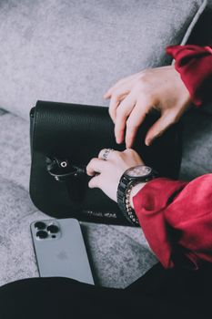 Stylish black leather handbag with a phone and hands in a vibrant setting.