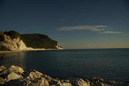 A Mountain Near the Body of Water Under the Blue Sky and White Clouds