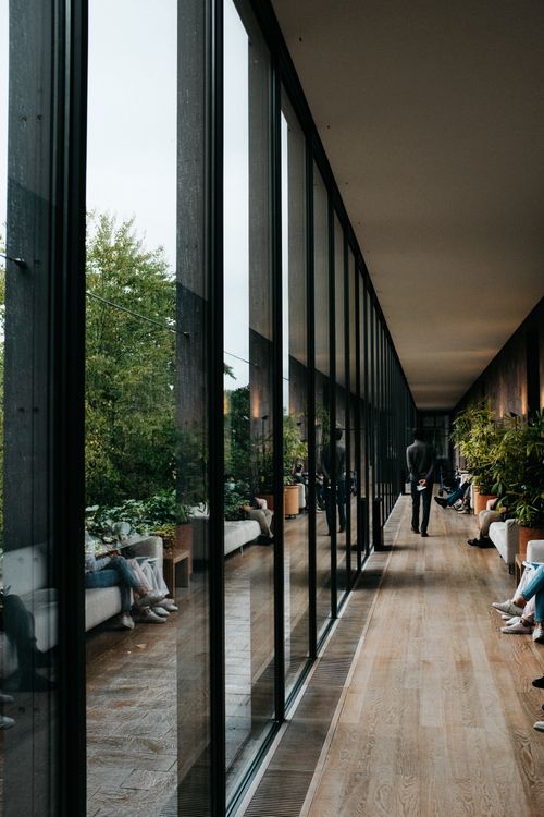 Free A spacious, modern corridor featuring a glass wall, wooden flooring, and lush greenery. Stock Photo
