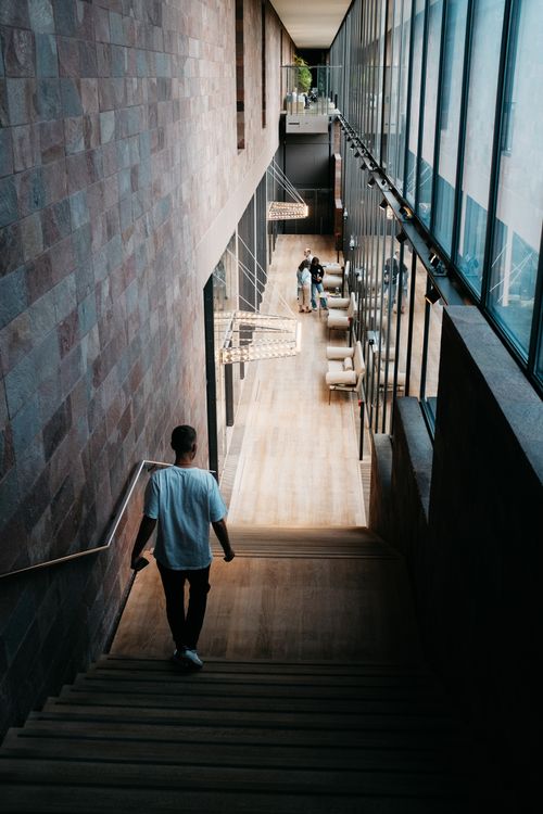Free A man descends a wooden staircase in a modern building with glass walls. Bright daylight setting. Stock Photo