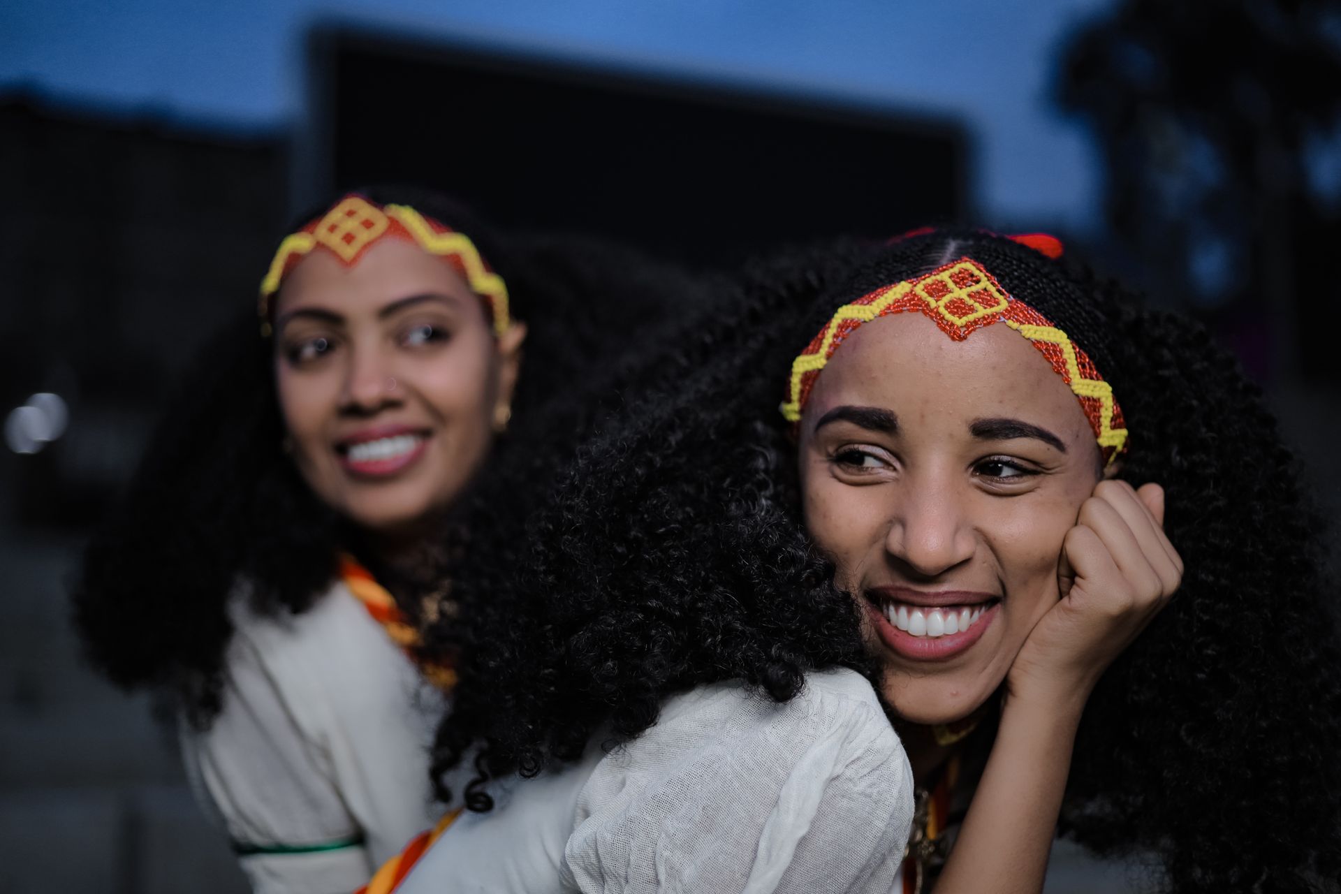 Two smiling women in traditional Ethiopian clothing and headbands, outdoors in Addis Ababa.