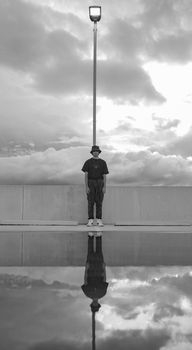 Man standing in front of street lamp reflecting in water, black and white.