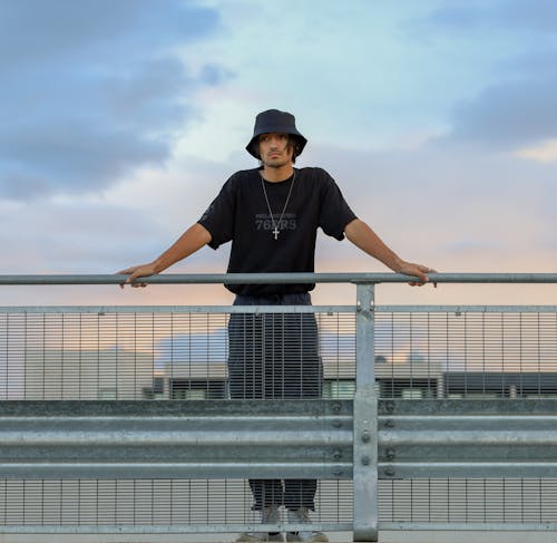 Man in Black Bucket Hat Standing Against Metal Railing