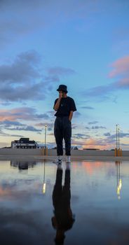 Man posing fashionably against a dramatic sunset sky with a reflection.