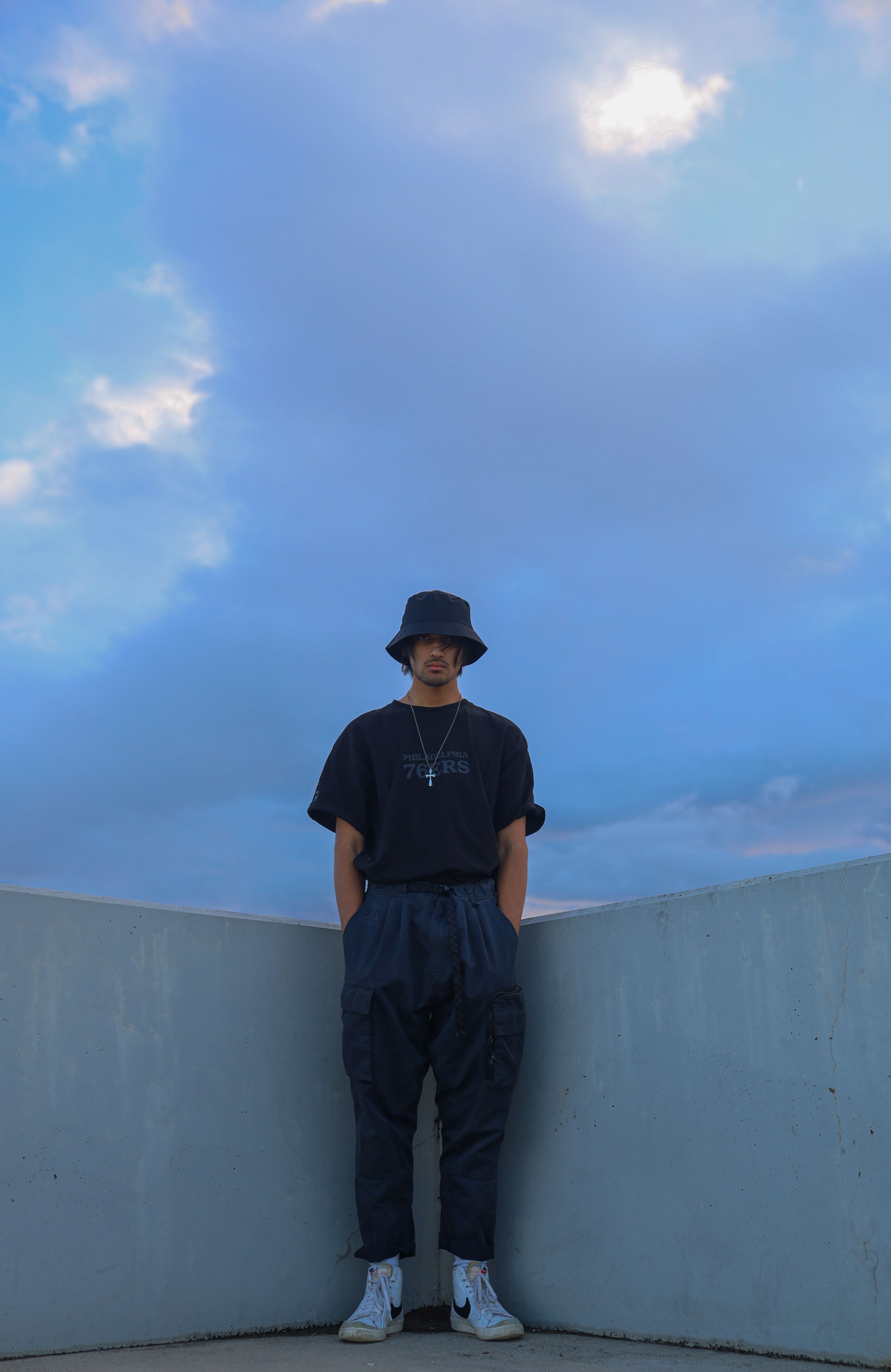 Jovem em streetwear posa contra um fundo de céu azul.