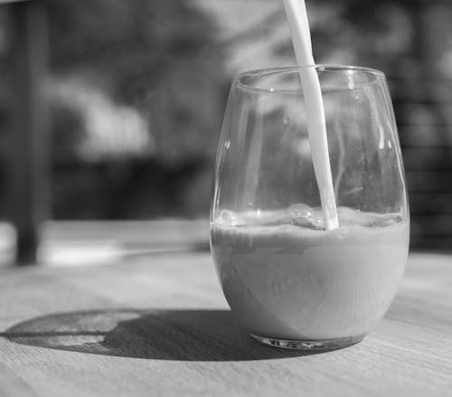 A Grayscale Photo of a Pouring Milk on Drinking Glass