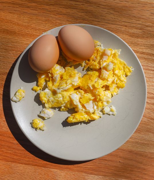 Plate of plain scrambled eggs beside whole eggs in natural light
