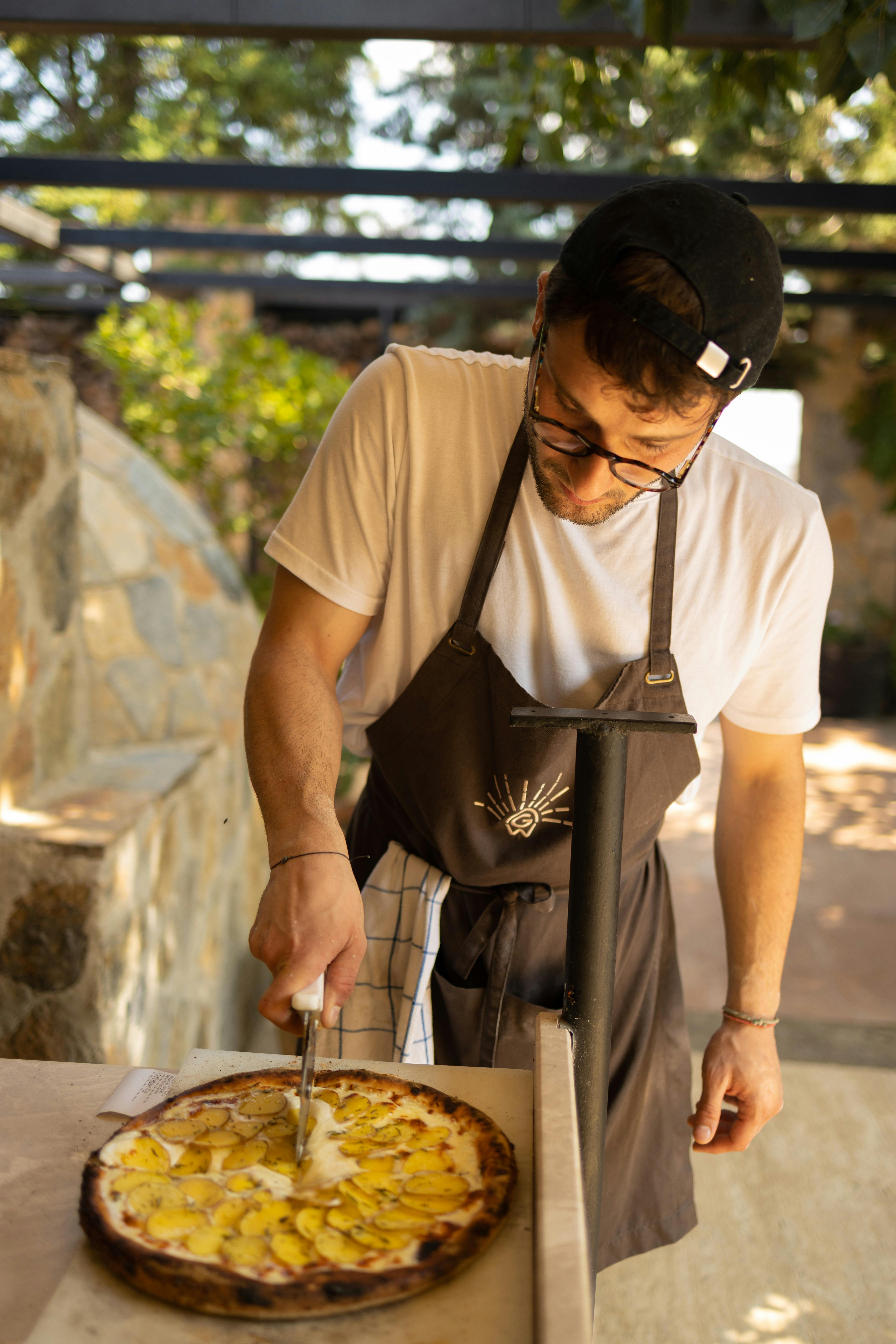 A young man in an apron slices a freshly baked pizza outdoors in Istanbul, Turkey.