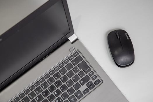 Overhead view of a laptop with a wireless mouse on a white table.