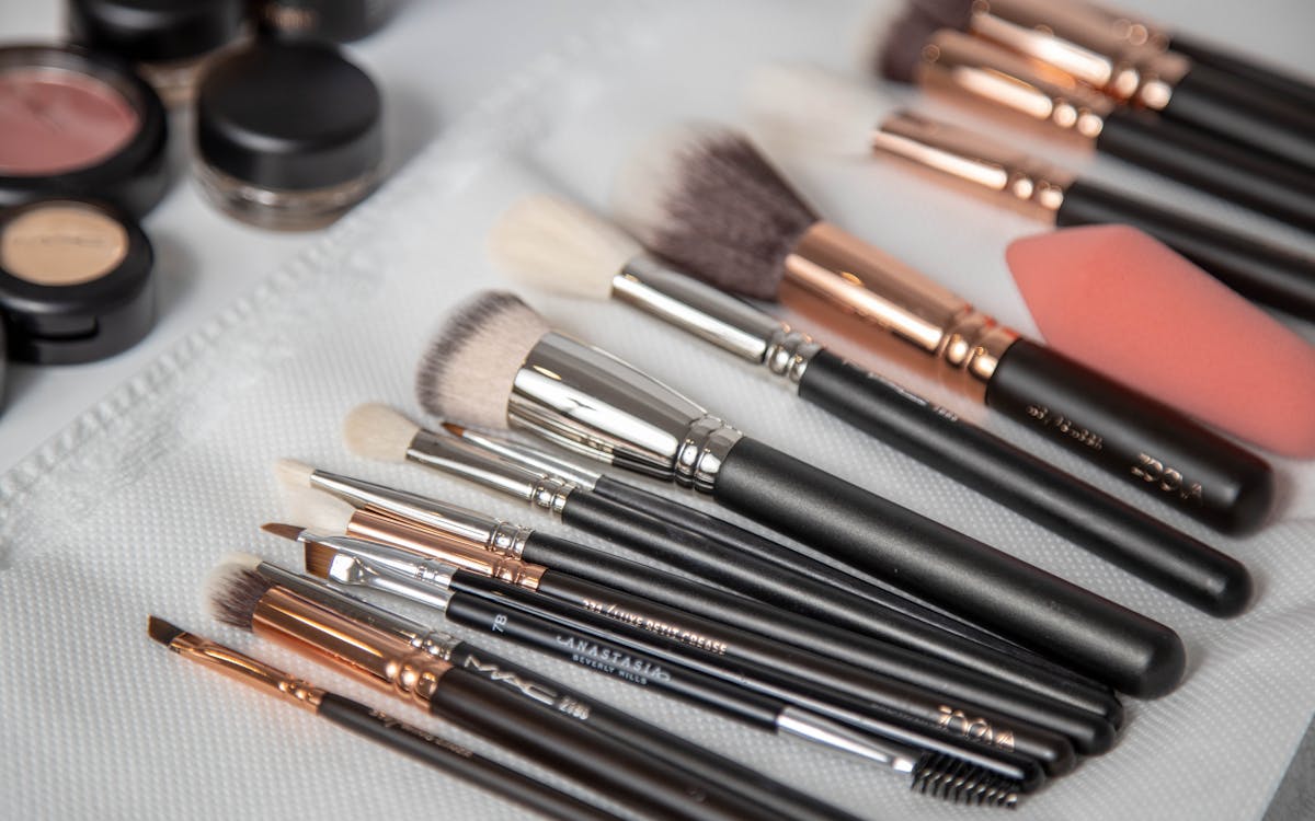 A collection of professional makeup brushes and tools arranged on a white towel with various cosmetic products.