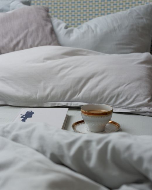 Inviting bedroom scene with soft linens, a book, and cup of tea on the bed.