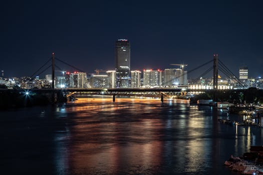 Explore this stunning cityscape featuring an illuminated bridge and skyscrapers reflecting on a tranquil river at night.