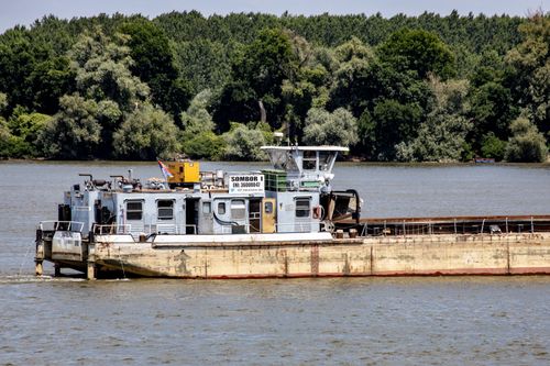 Free A large barge on a calm river against a lush forest backdrop. Stock Photo