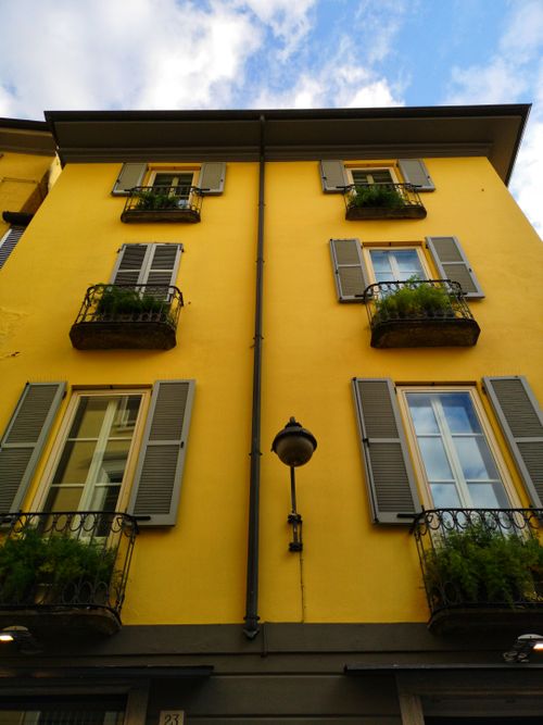 Free Bright yellow building facade with green window shutters in Italy, seen from below. Stock Photo