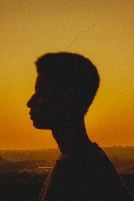 Captivating silhouette of a man in profile against a stunning yellow-orange sunset sky.