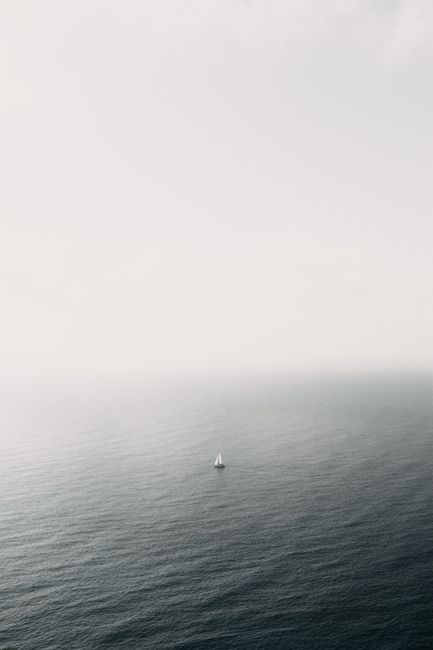 A lone sailboat on a calm ocean with a misty horizon, capturing serene and minimalist beauty.