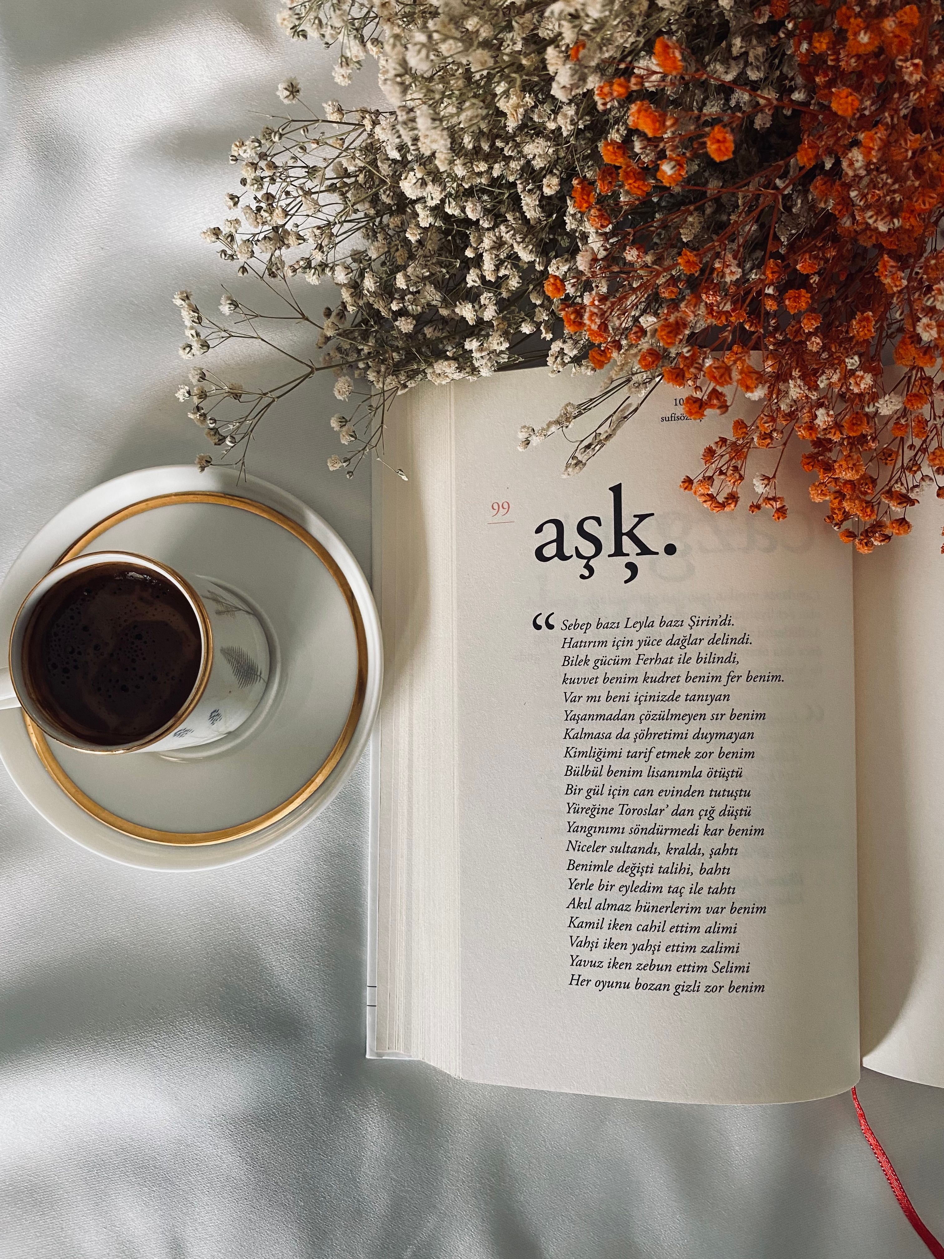 High angle view of a coffee cup, book, and flowers on a white surface.