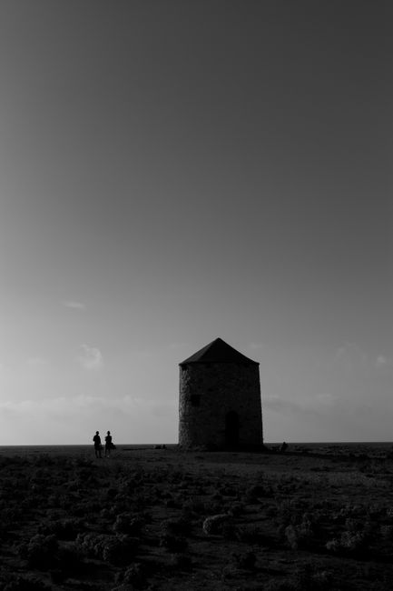 Black and white image of two people near a windmill in a rural landscape.