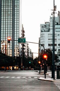 City intersection with illuminated traffic lights at dusk. Tall buildings line the urban street.