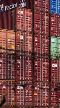 Vertical shot of colorful, stacked shipping containers at a bustling cargo port.