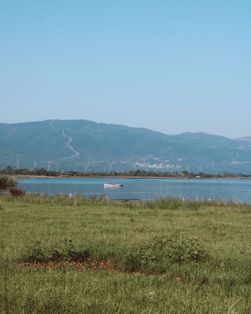Free Peaceful view of a boat on a lake, surrounded by green fields and distant mountains under a clear blue sky. Stock Photo
