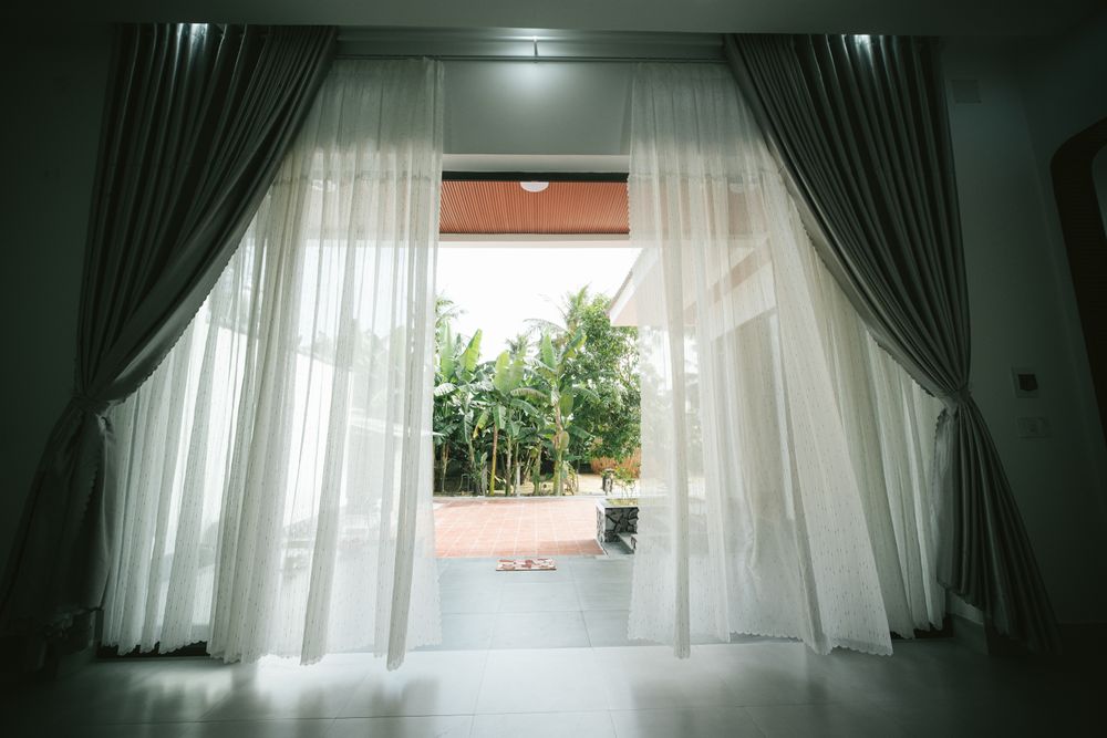 A garden seen through open curtains from inside a room — photo by Pew Nguyen on Pexels