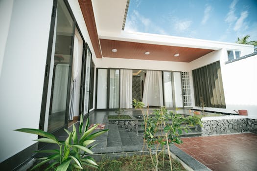 Contemporary house with glass doors, plants, and terrace under a clear sky.