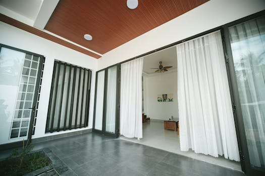 Contemporary interior view featuring sliding glass doors and white curtains leading to a cozy room.