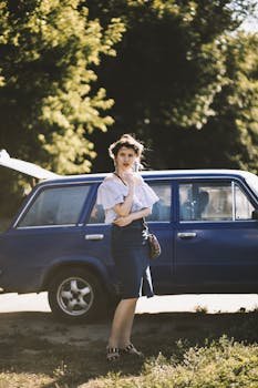 一名女子自信地站在一辆蓝色古董车旁，阳光明媚