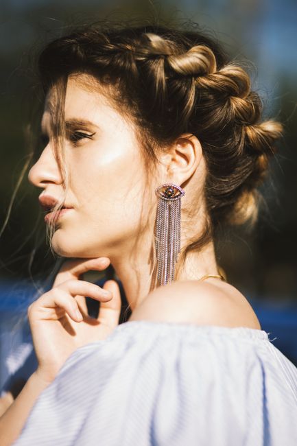 Side view of a stylish young woman outdoors with braided hair and a statement earring in the sunlight.