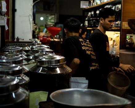 Two men working in a busy coffee shop surrounded by jars and equipment.