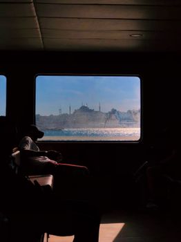 Silhouette of passengers with Istanbul's skyline seen through a ferry window.