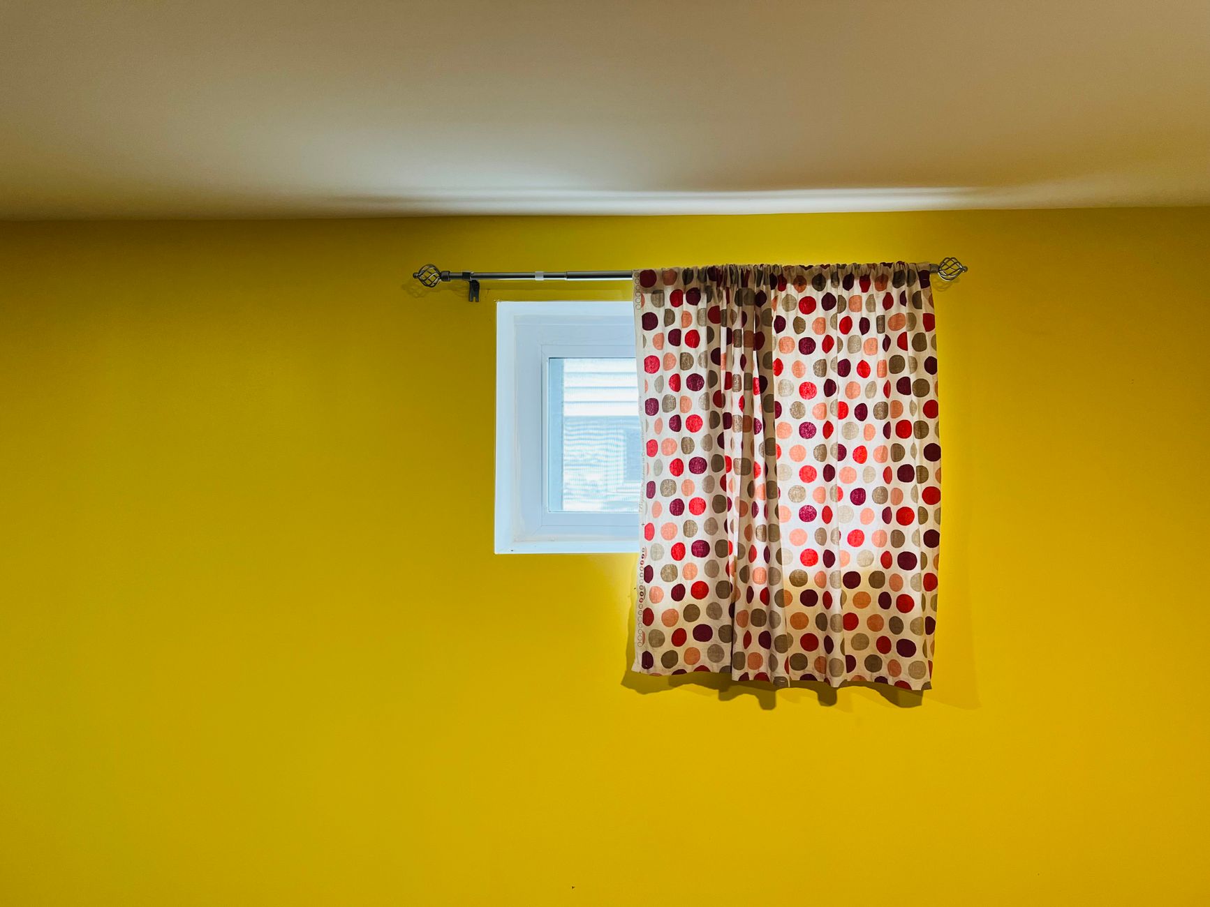 窗簾顏色太深壓迫感強?6招輕鬆降低空間壓抑 A vivid yellow wall featuring a window adorned with red and black polka dot curtains.