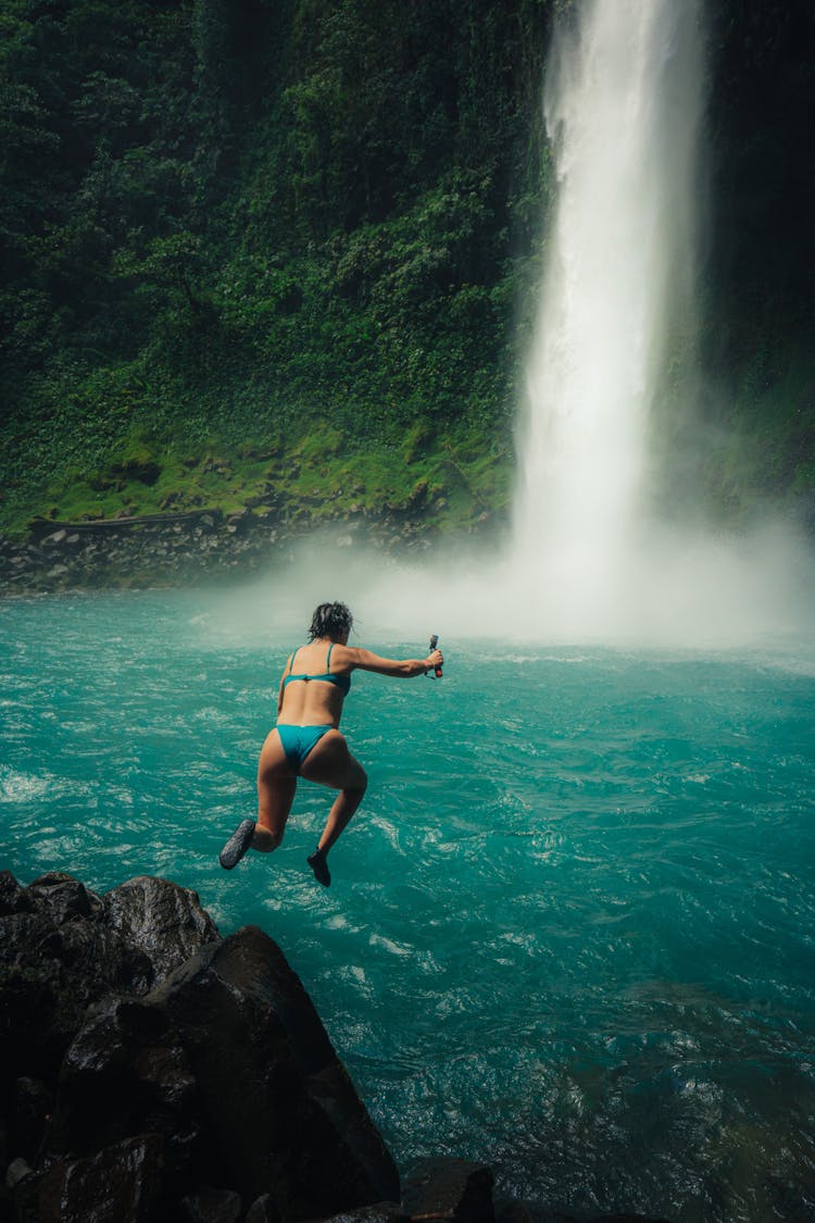 Woman Jumping From A Cliff Into A Waterfall 