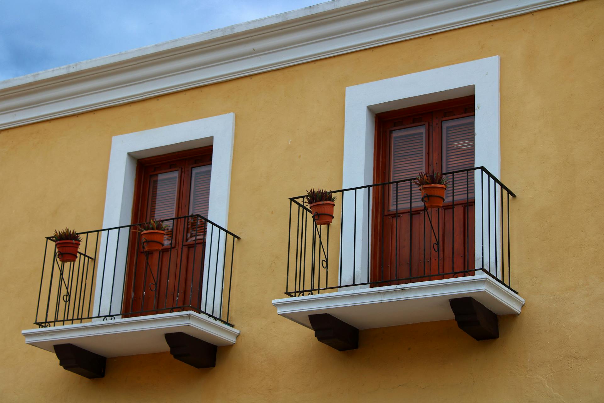 Colorful yellow building facade in Valladolid, Mexico featuring twin balconies with potted plants.