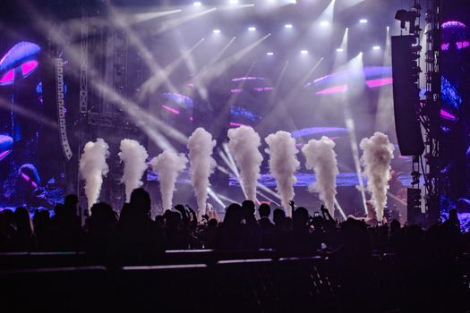 Silhouettes of a crowd enjoying a lively night concert with vibrant lights and smoke effects.