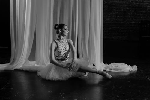 Free A serene black and white portrait of a ballerina sitting gracefully in a studio with curtains. Stock Photo