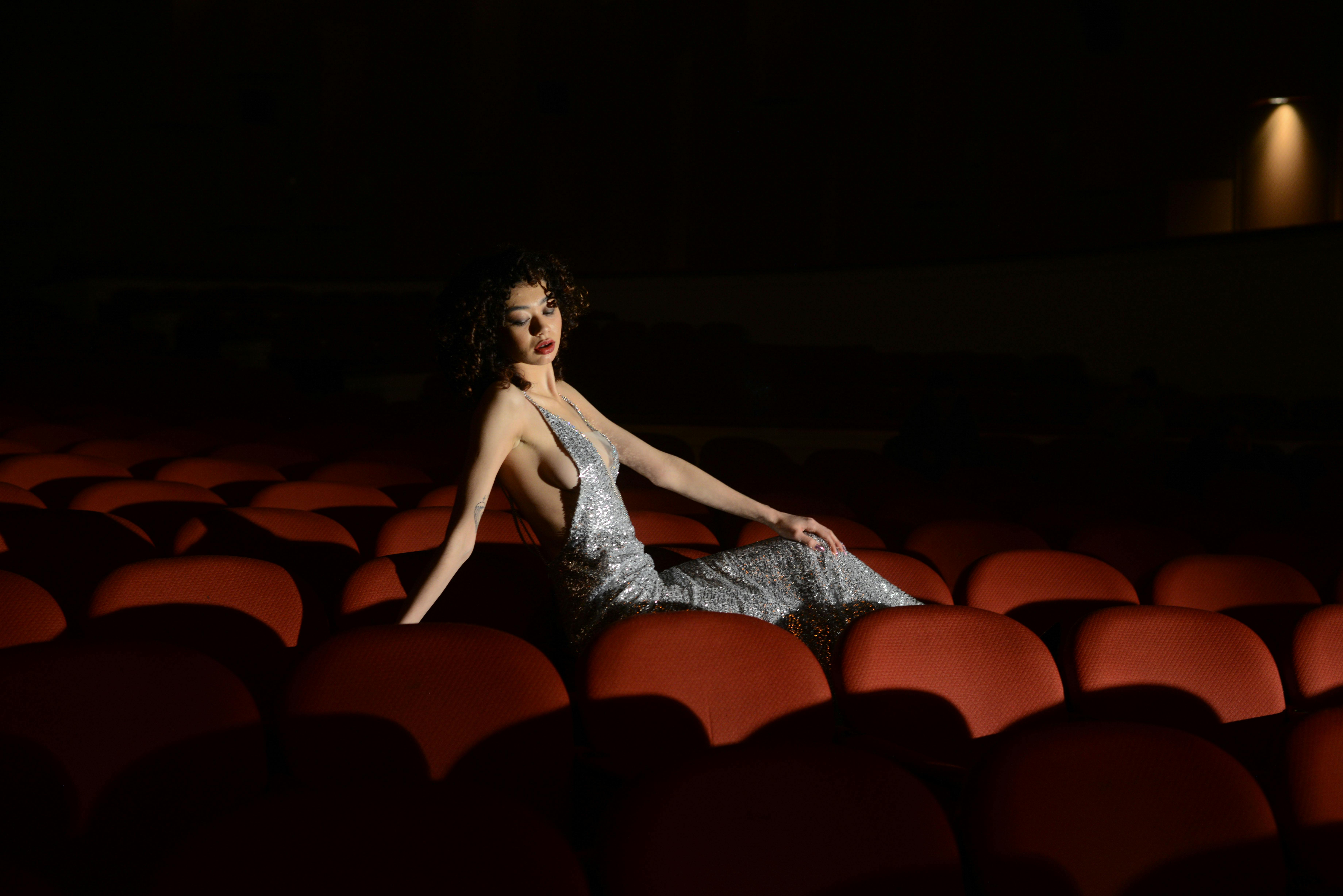 Free Elegant woman in silver dress sitting in a dimly lit theatre, Mar del Plata, Argentina. Stock Photo