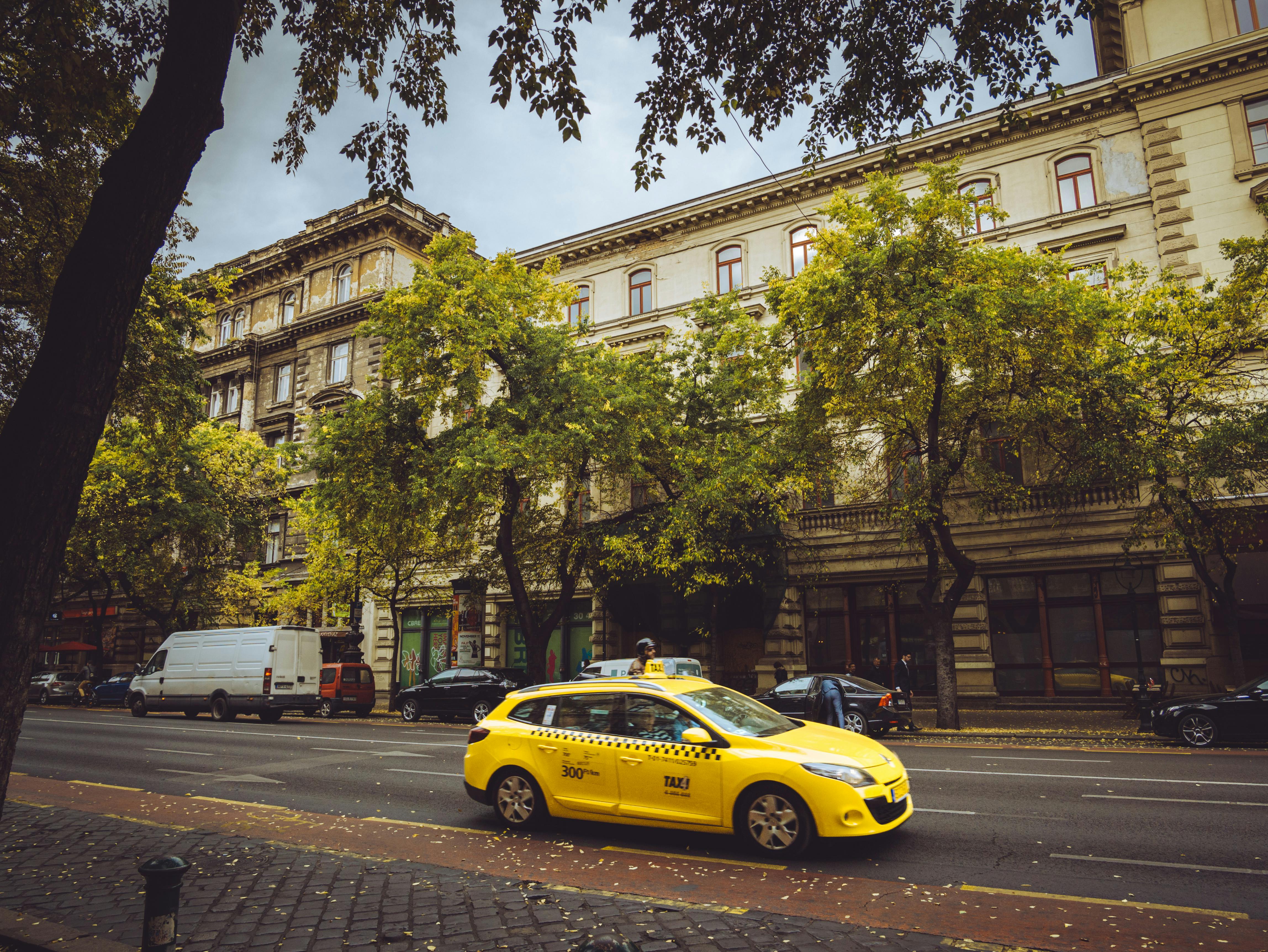 A vibrant yellow taxi driving past historic buildings in Budapest, Hungary.