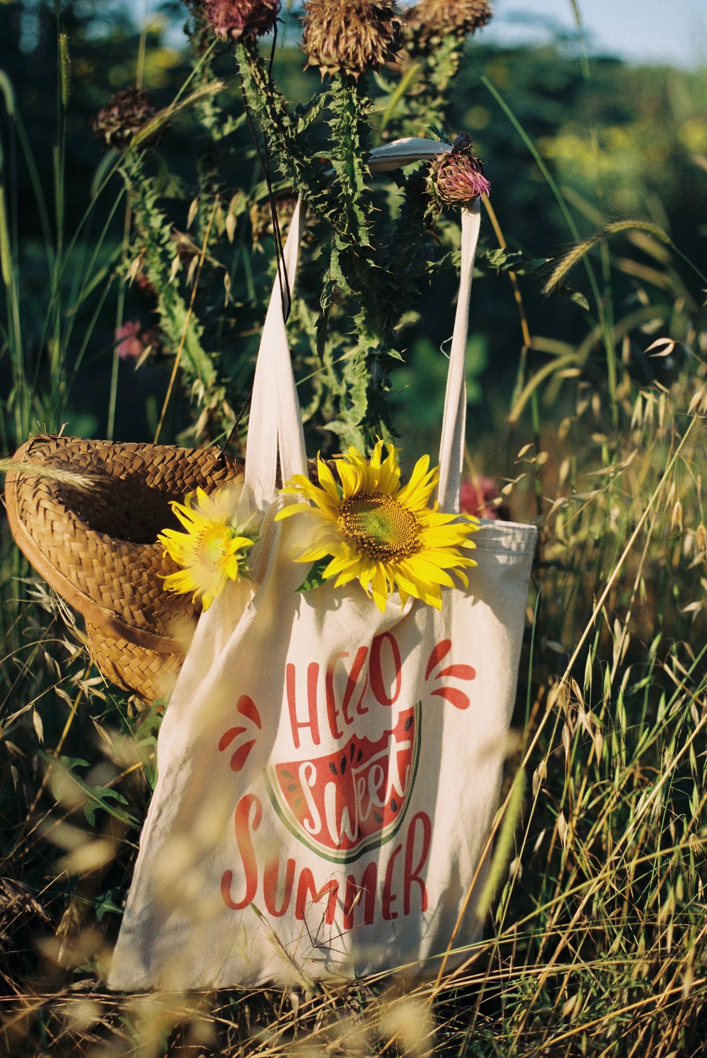 Rustic tote with 'Hello Sweet Summer,' filled with sunflowers amidst a meadow.