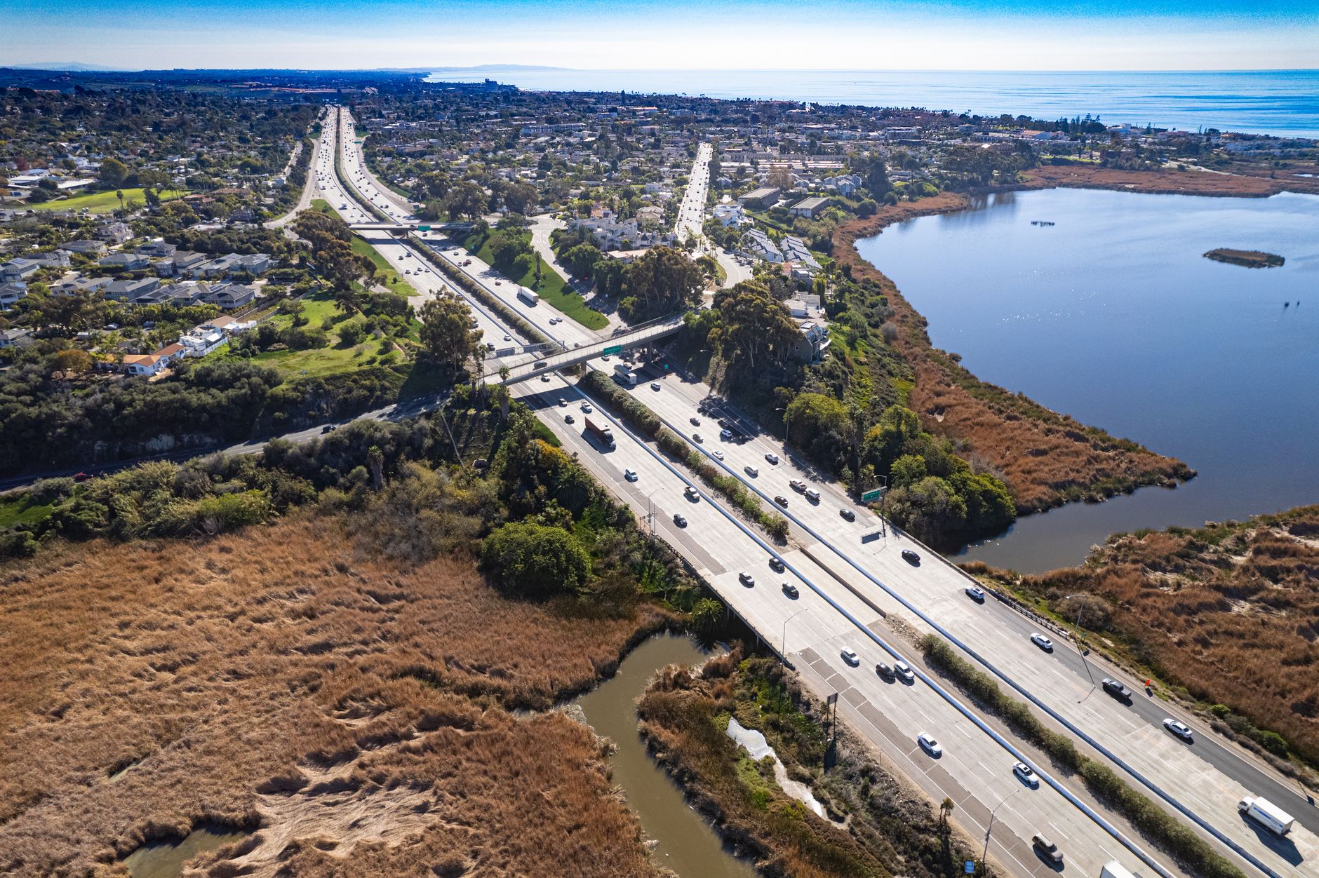 Aerial shot of Carlsbad's scenic highway with adjacent lagoon under a clear blue sky.