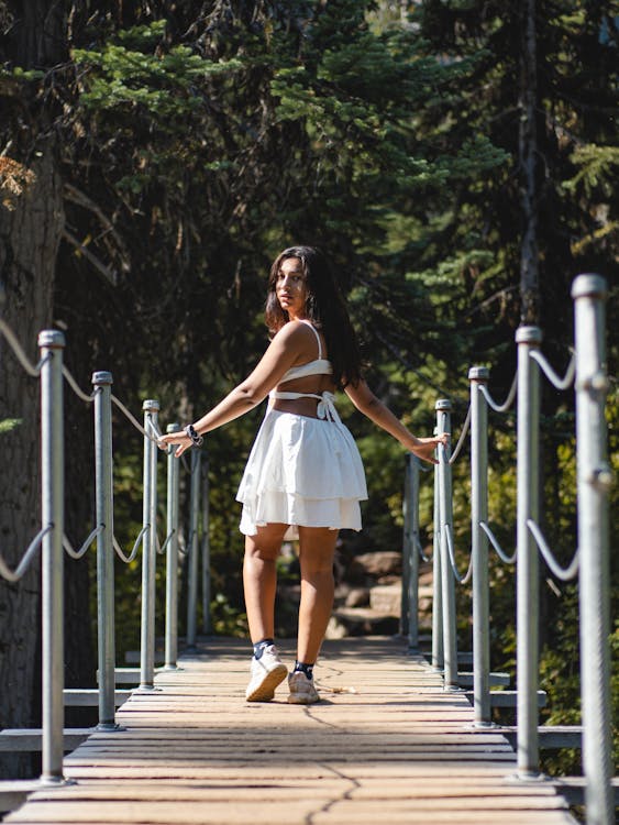 A Woman in White Dress Walking on a Wooden Bridge while Looking Over Shoulder