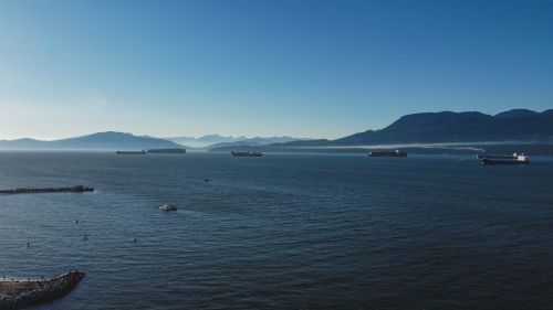 Free Panoramic view of Vancouver's Burrard Inlet with ships and distant mountains under a clear blue sky. Stock Photo
